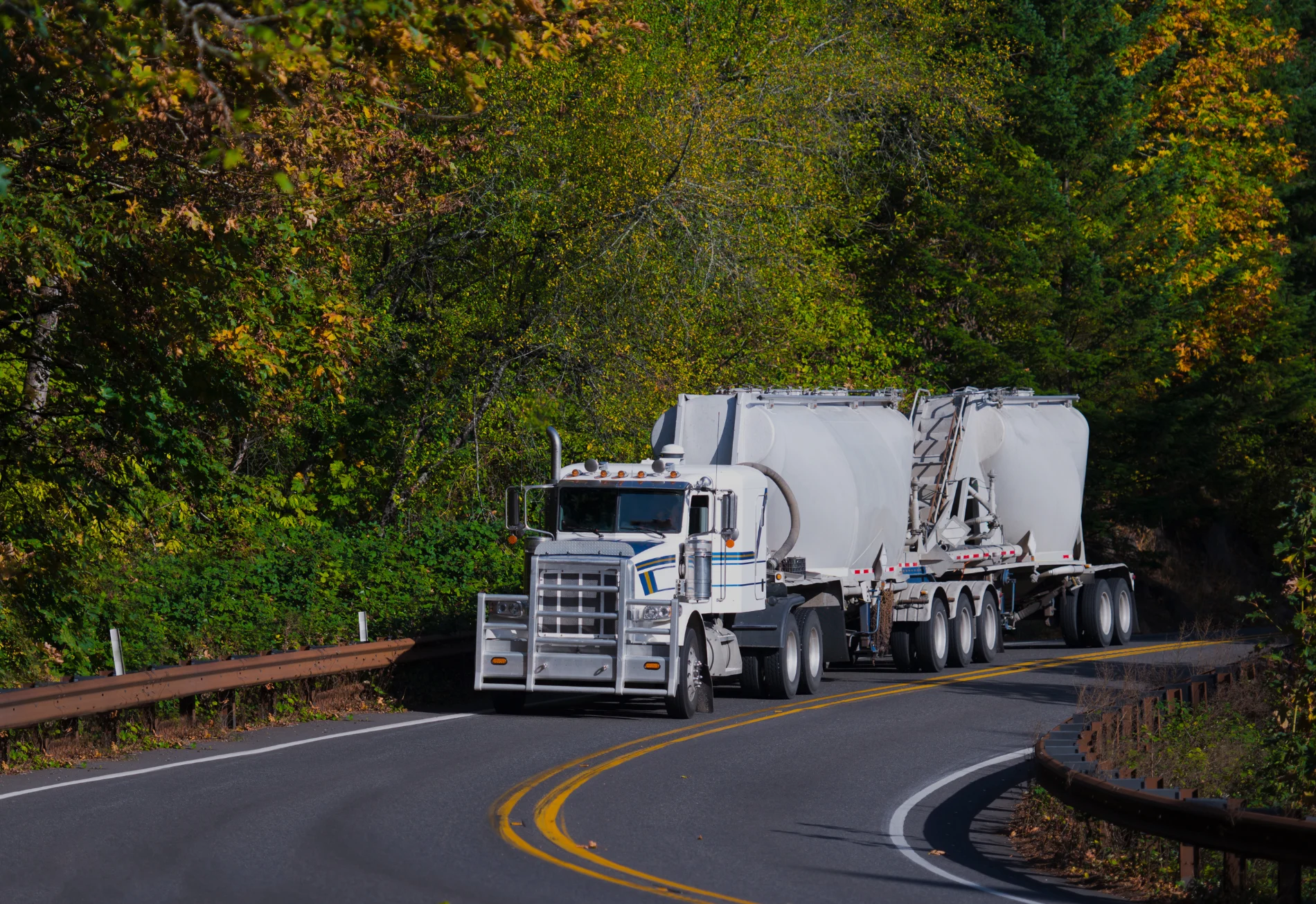 Long haul Semi Truck bulk trailers on autumn winding road